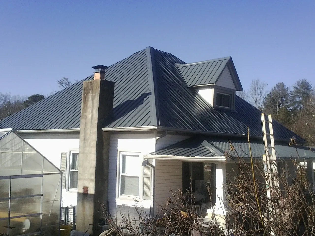 Dark blue standing seam metal roof on a white farmhouse with dormer — Slate & Tile Roof Repair by Roofing Brothers in Sand Springs