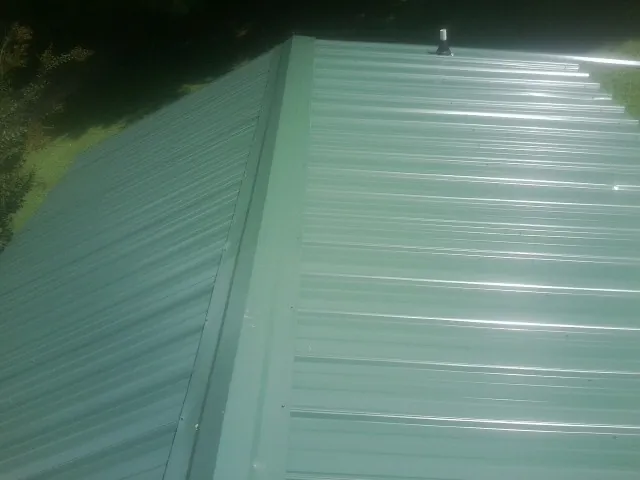 New green metal panels meeting at the ridge of a roof — Flat Roof Repair work by our crew in Sand Springs