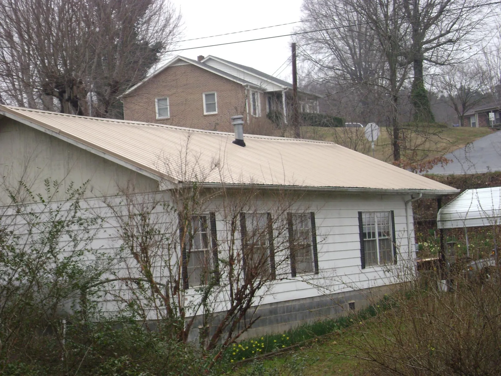 Tan metal roof on a white sided house set into a hillside — Commercial Roofing by Roofing Brothers in Sand Springs