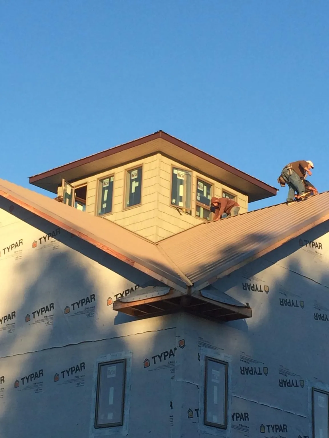 Roofers working around a rooftop cupola on a new metal roof at sunset — Roof Waterproofing in Sand Springs by Roofing Brothers